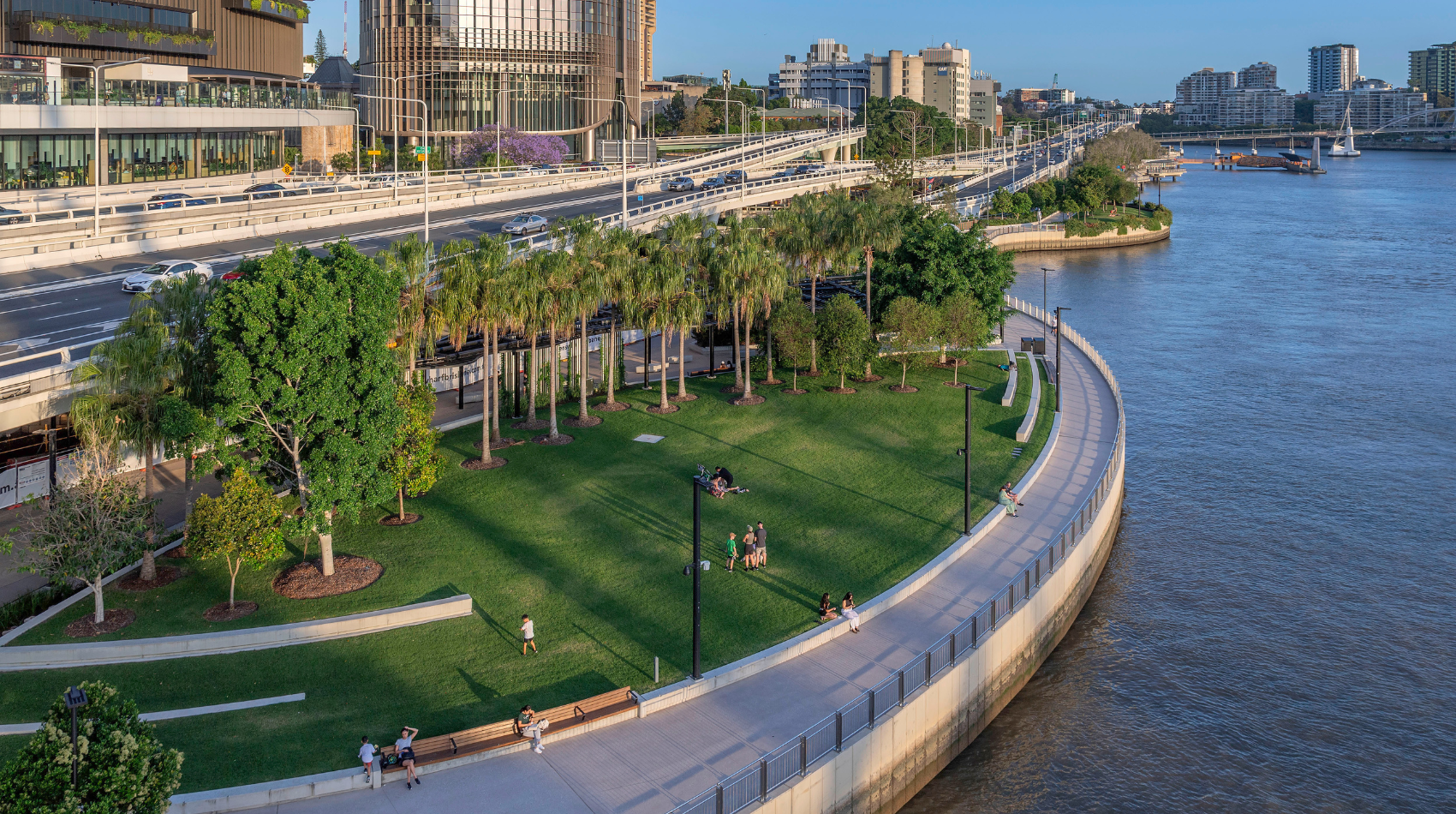 An aerial shot of a green grassy space and walkway next to the Brisbane River.