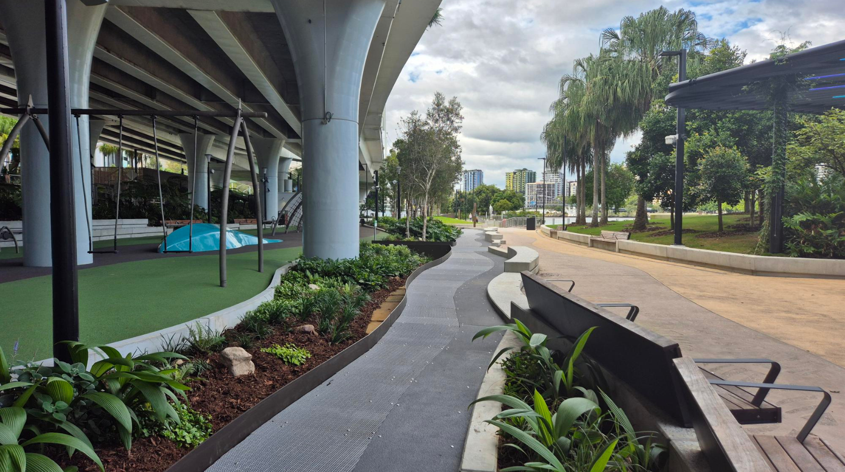 An outdoor playground and walkway near a river and grassy area.
